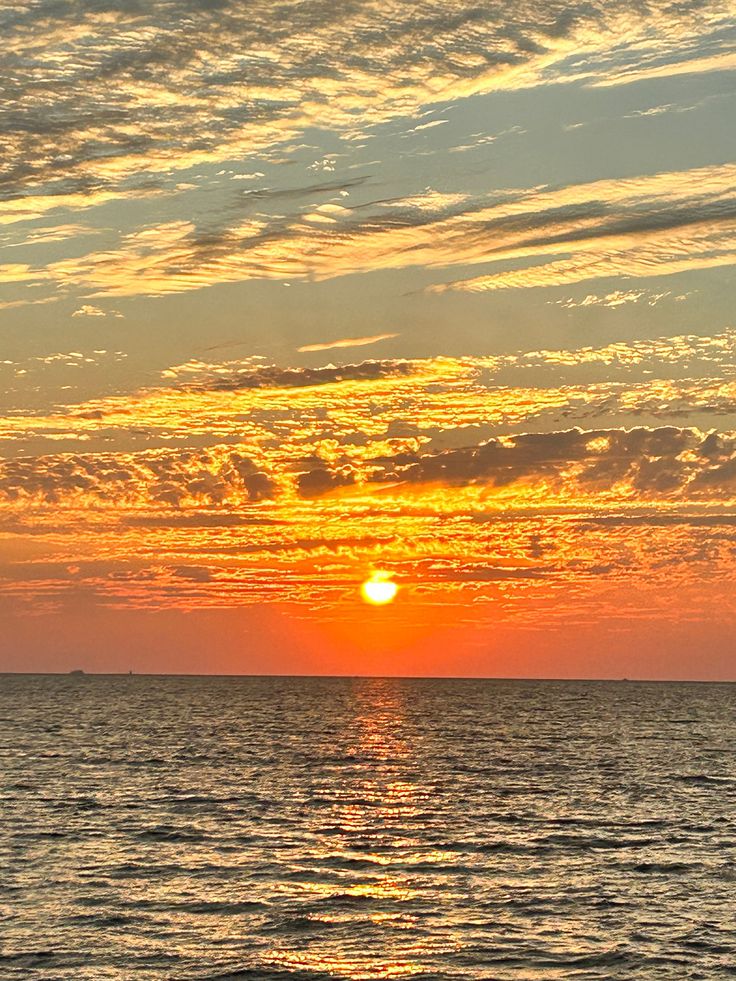 the sun is setting over the ocean with clouds in the sky