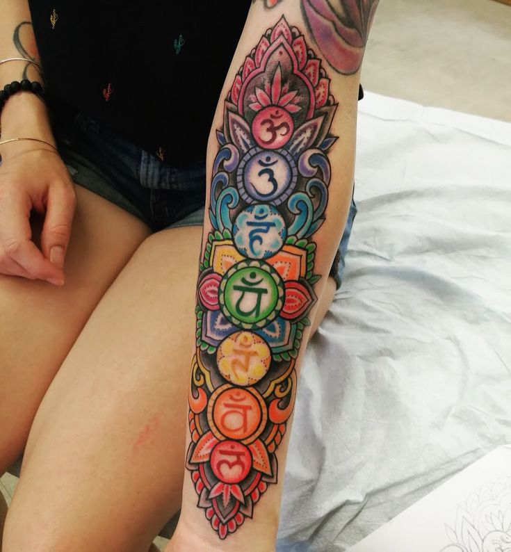 a woman with a colorful tattoo on her arm sitting on a bed next to a book