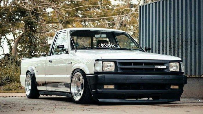 a white truck parked in front of a metal structure with trees behind it and the words gen's written on its hood