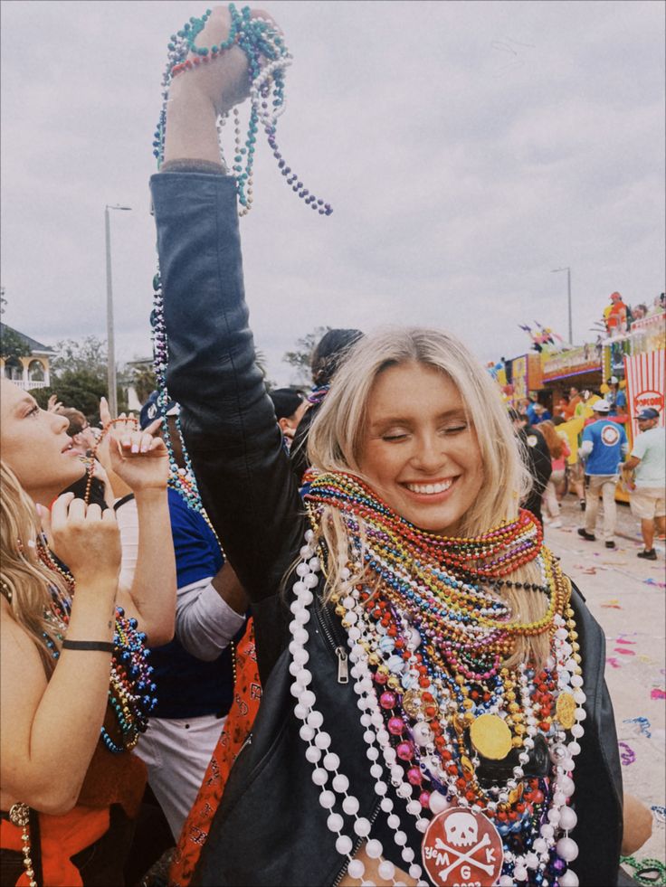 a woman is holding up her hand with beads all around her neck and hands in the air