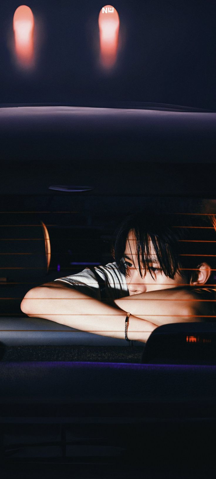 a woman laying in the back of a car at night with her arm on her head