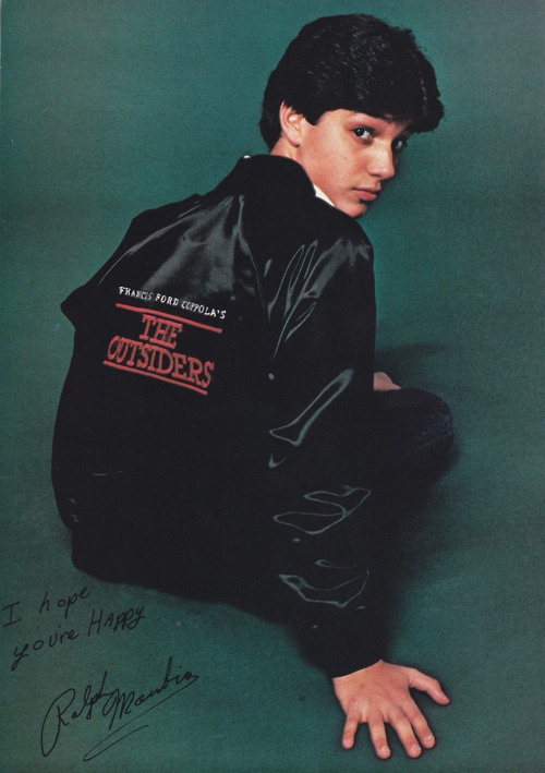 a young man sitting on the ground wearing a jacket