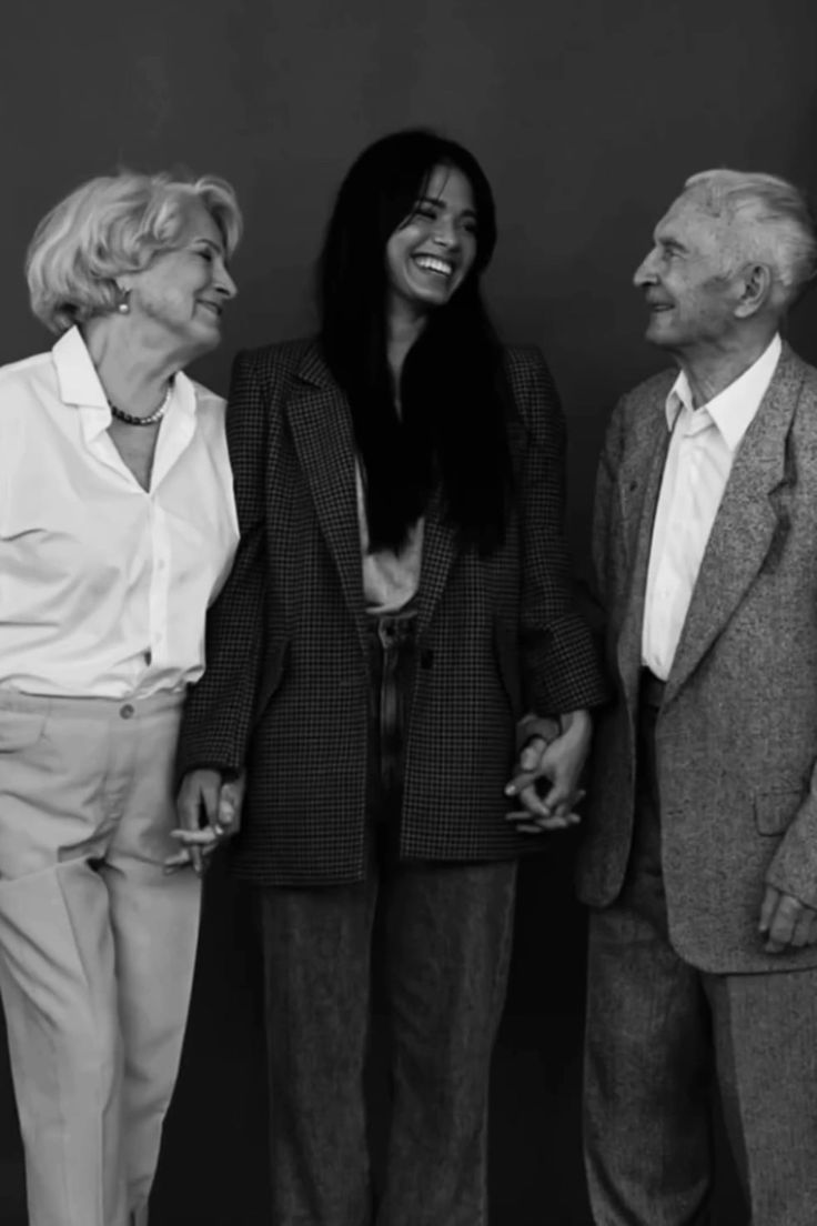 three people standing next to each other in front of a black and white photo with one woman holding the hand of another man