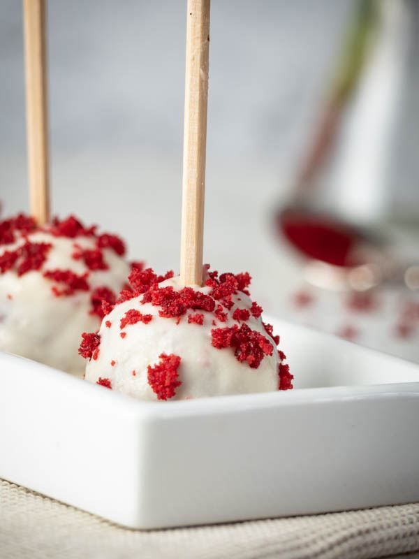 two red and white desserts on sticks in a square dish with sprinkles