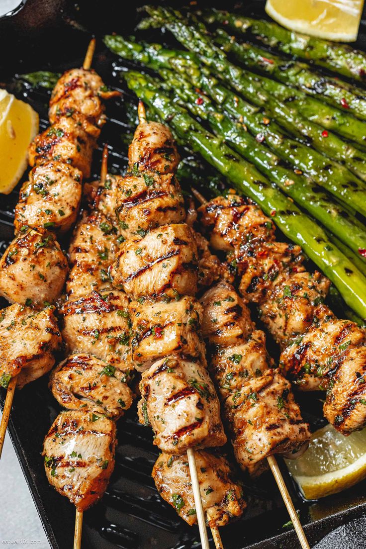 chicken and asparagus skewers on a grill with lemon wedges in the foreground