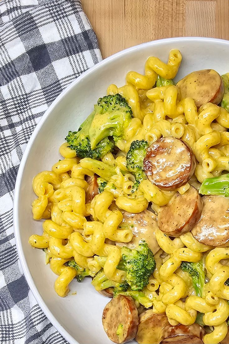 a white bowl filled with macaroni and broccoli on top of a checkered table cloth