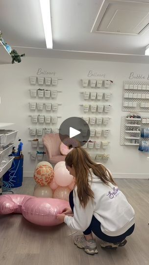 a woman kneeling down to pick up balloons in a room filled with shelves and chairs