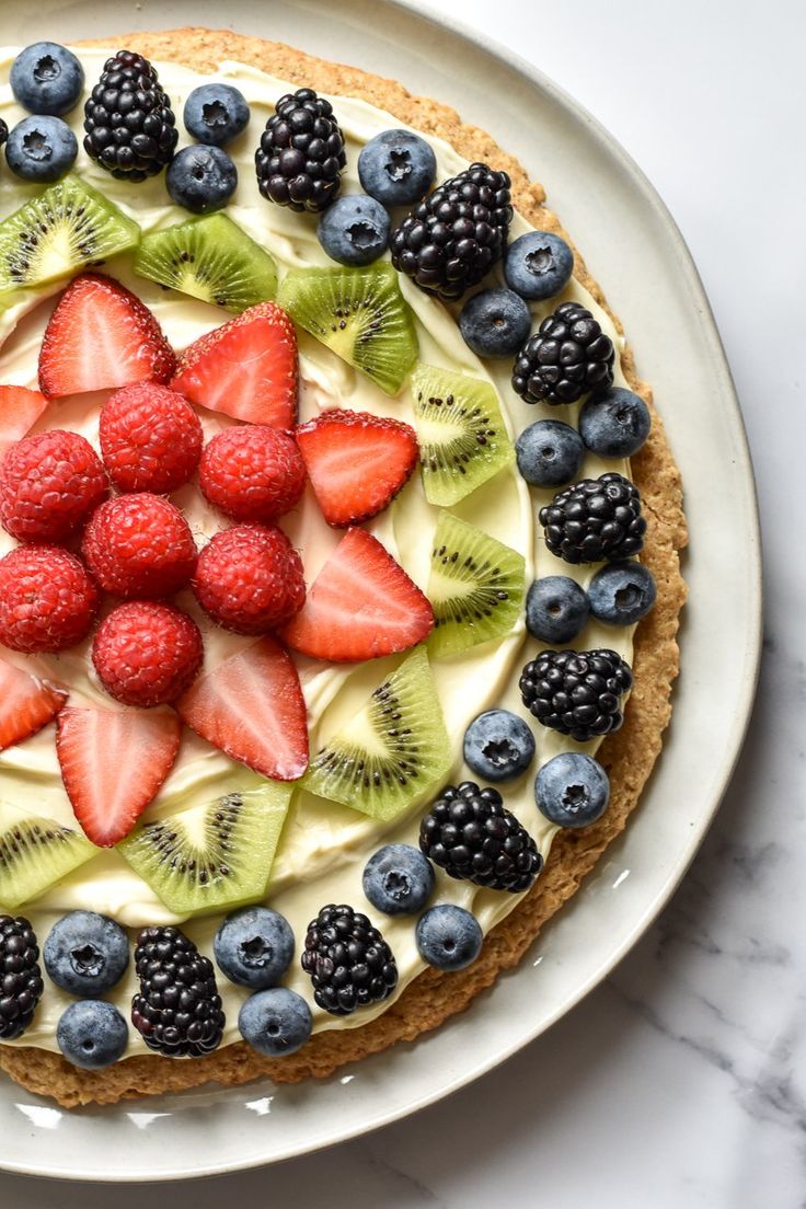 there is a pie with fruit on the top and blueberries, raspberries, kiwis, and strawberries