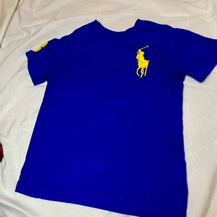 Blue Polo T-Shirt With Yellow Logo Never Worn 100% Cotton Blue Crew Neck Polo Shirt For Summer, Blue Graphic Tee With Logo Print, Blue Short Sleeve Shirt With Logo Print, Blue Cotton Polo Shirt With Graphic Print, Blue Graphic Tee With Crew Neck, Blue Crew Neck Top With Logo Print, Blue Crew Neck Shirt With Logo Print, Blue Casual Crew Neck Polo Shirt, Blue Casual Polo Shirt With Crew Neck