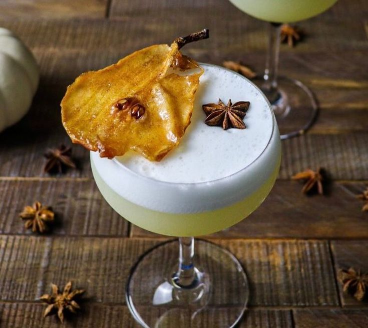 two glasses filled with an alcoholic drink on top of a wooden table next to pumpkins