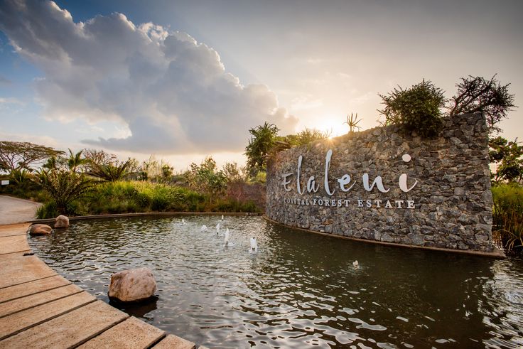 the entrance sign to an exotic resort with water and trees in the background at sunset