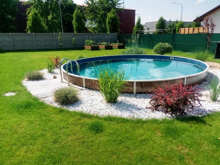 a pool in the middle of a yard with gravel around it and plants growing on either side