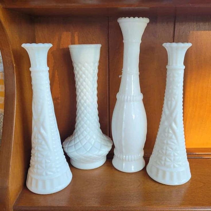 three white glass vases sitting on top of a wooden shelf next to each other