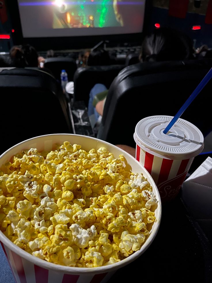 a bowl of popcorn and a drink on a table in front of a movie screen