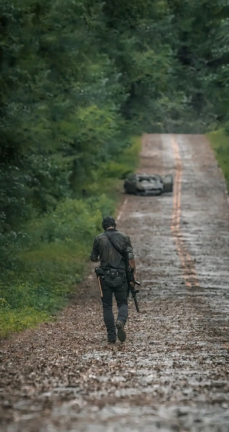 a man with a backpack walking down a dirt road in the woods next to cars