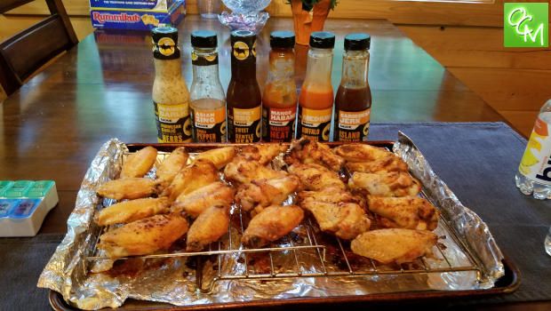 some chicken wings are sitting on tin foil near bottles of sauces and water at a table