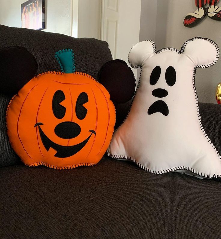 two halloween pillows sitting on top of a couch next to a pillow shaped like mickey mouse