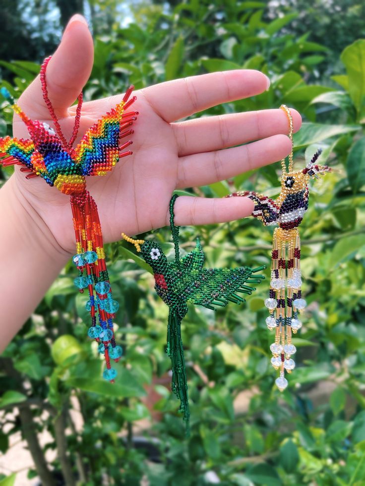 a person's hand holding three beaded bird ornaments in front of green plants