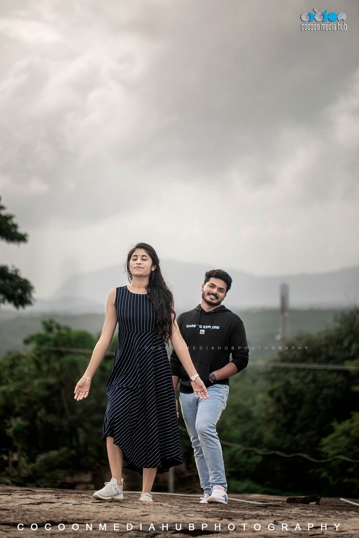 a man and woman standing on top of a dirt hill with trees in the background