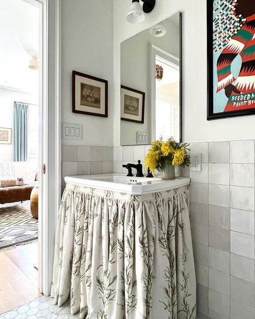 a white sink sitting under a mirror in a bathroom next to a painting on the wall