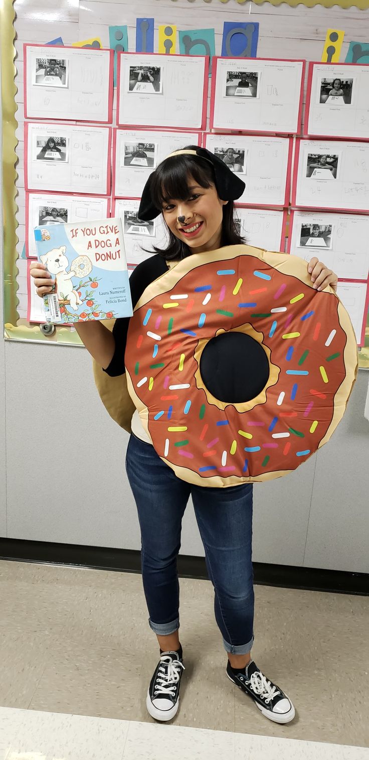 a woman holding up a giant donut shaped book in front of a bulletin board