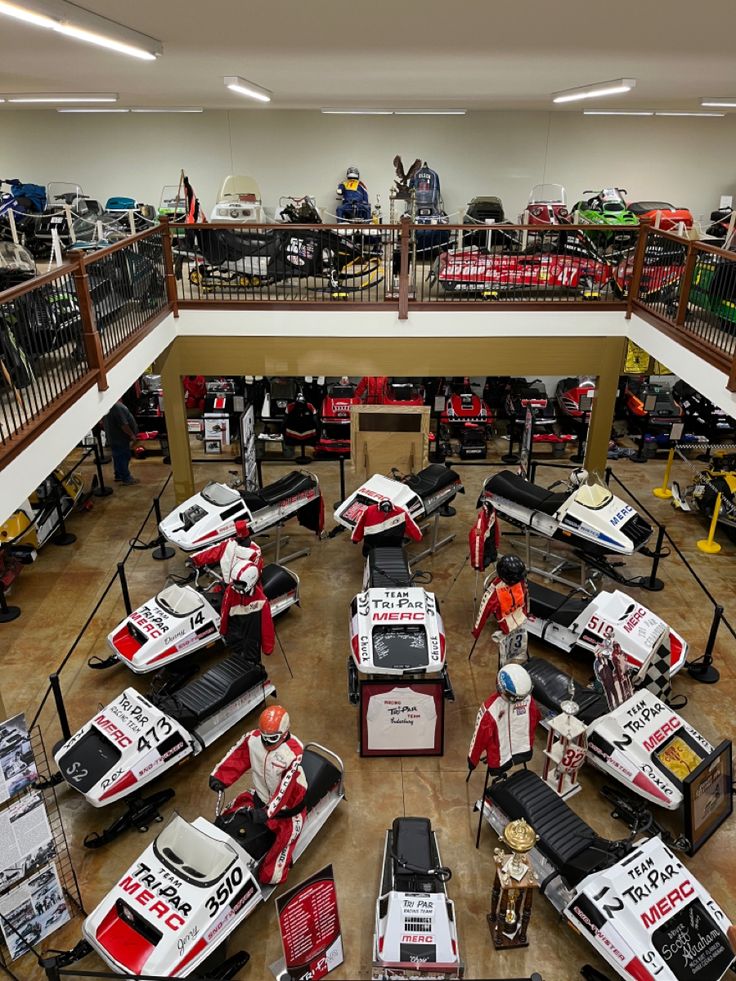 a room filled with lots of different types of racing cars and people working on them