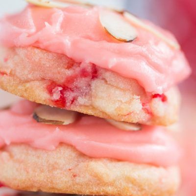 two cookies with pink icing and almonds stacked on top of each other