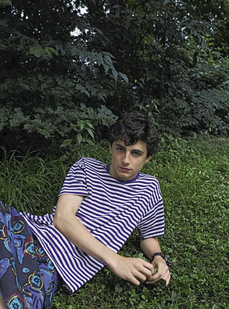 a man laying on the ground in front of some bushes and trees with his hand under his leg