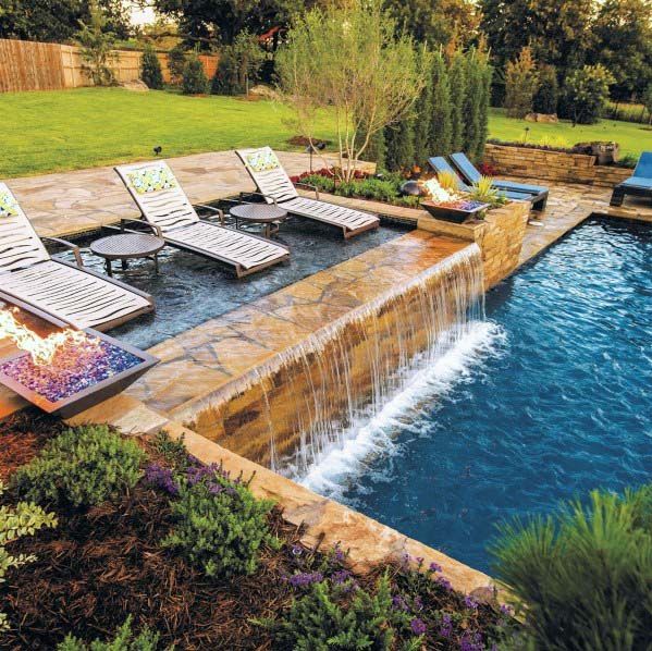 an outdoor pool with lounge chairs next to it and a waterfall running down the side