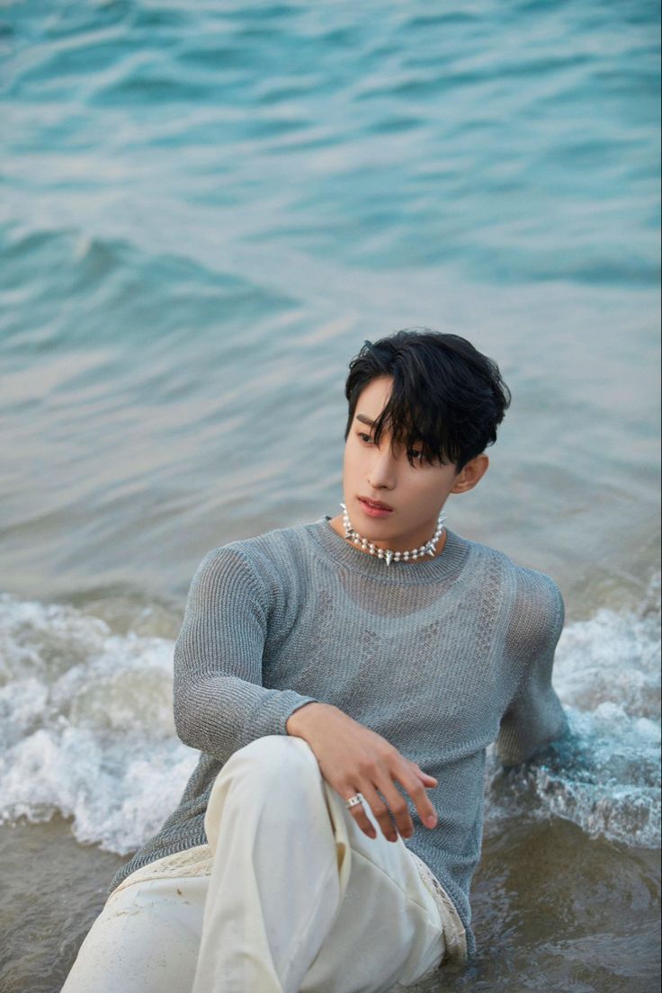 a young man sitting in the water with his hand on his hip and looking off into the distance