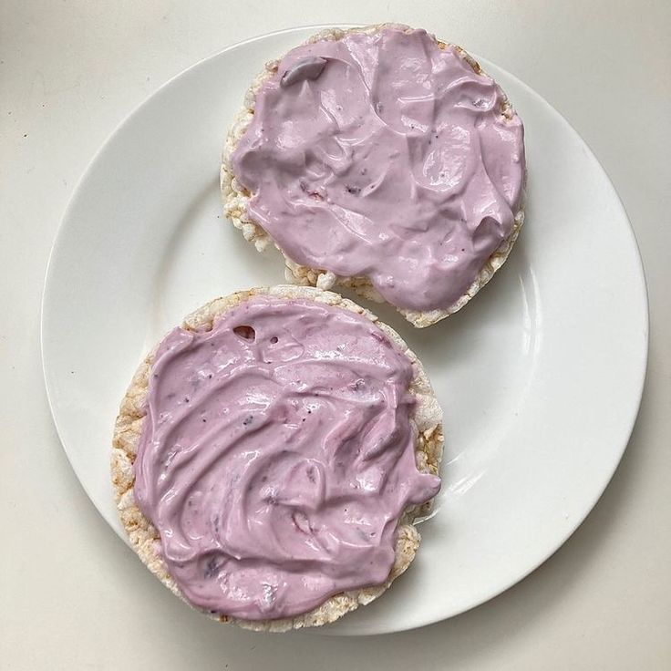 two pieces of bread topped with purple icing on top of a white plate next to a cup of coffee