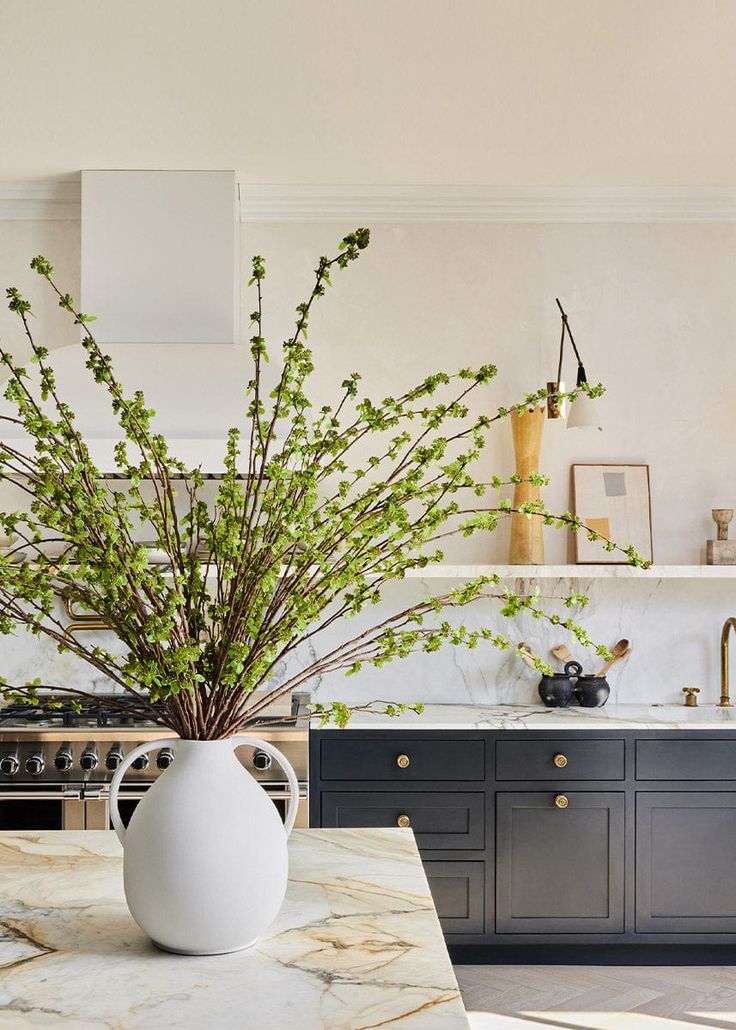 a white vase filled with green plants on top of a kitchen counter next to an oven