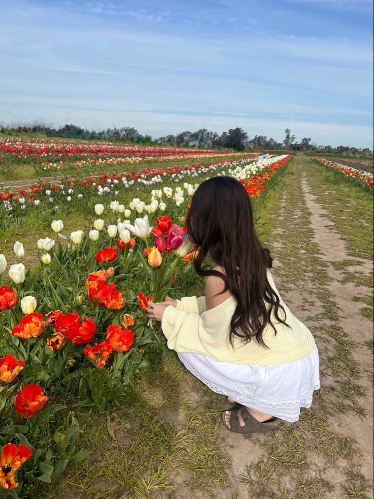 a woman kneeling down in front of a field full of flowers