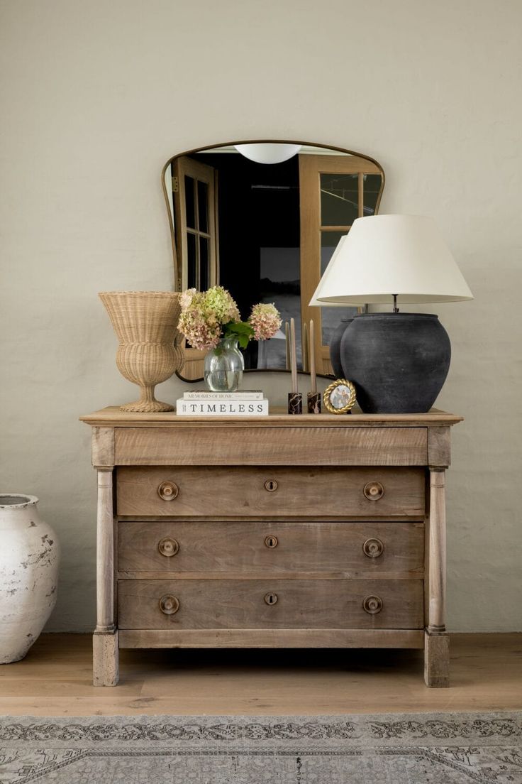 a dresser with a mirror, lamp and vase on it in front of a wall