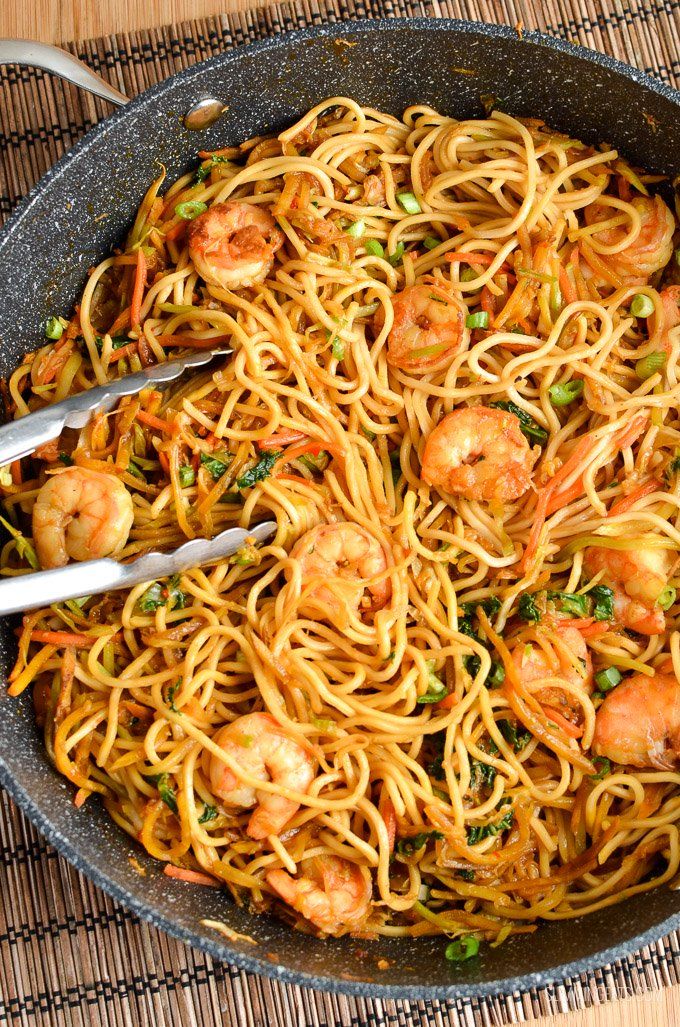 shrimp and noodle stir fry in a skillet with tongs