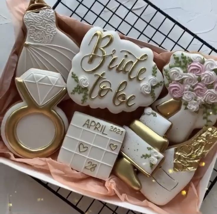 wedding cookies are arranged in a box on a wire rack with pink and gold decorations