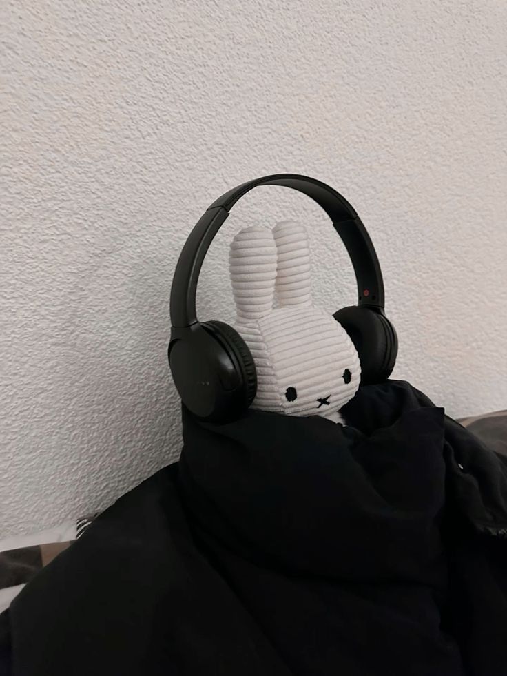 a stuffed animal wearing headphones on top of a black blanket in front of a white wall