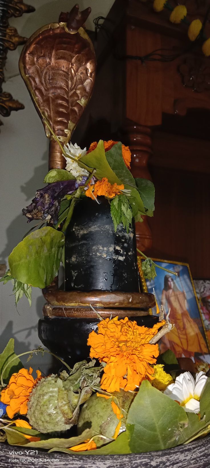 an arrangement of flowers and leaves in a vase on top of a table with pictures