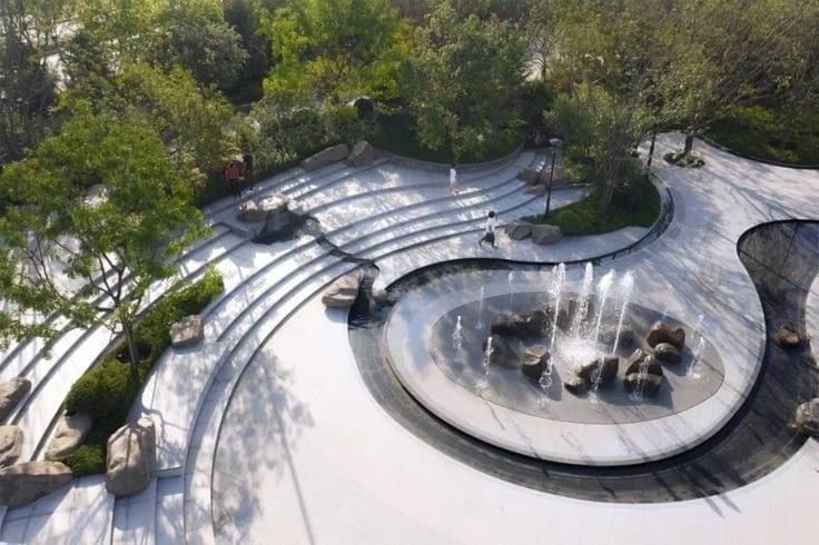 an aerial view of a park with water fountains and rocks in the foreground, surrounded by trees