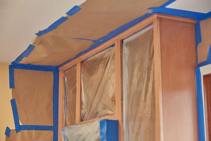 an unfinished room with blue tape on the walls and wood cabinets in place for painting