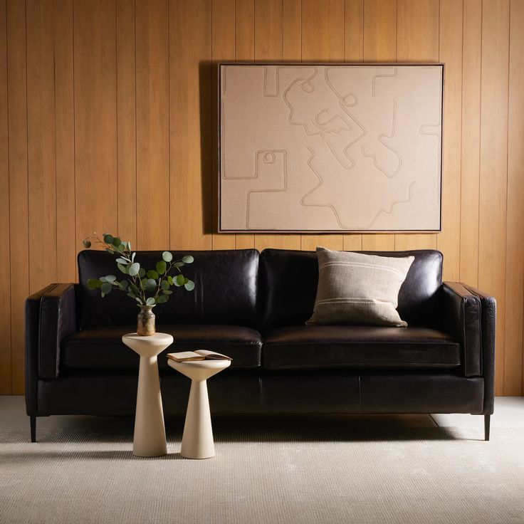 a black leather couch sitting next to a table with a vase on it