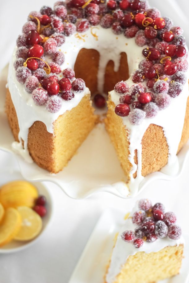 a cake with white frosting and cranberries is on a plate next to sliced lemons