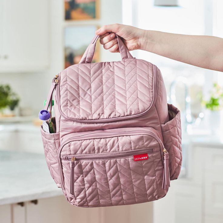 a woman holding a pink quilted backpack in her hand