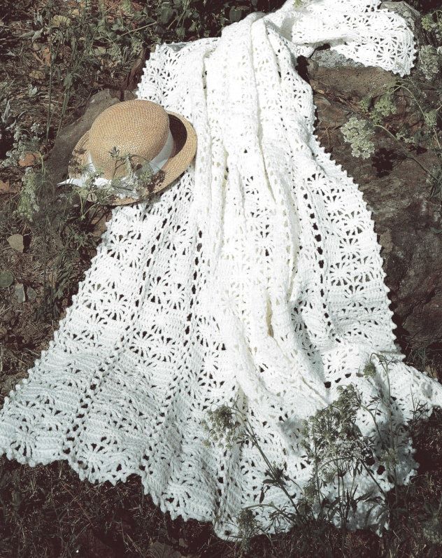 a white crocheted blanket and hat on the ground