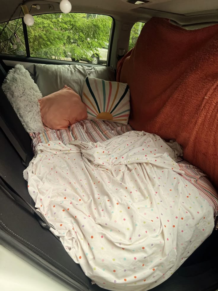 a baby sleeping in the back of a car with blankets and pillows on it's side