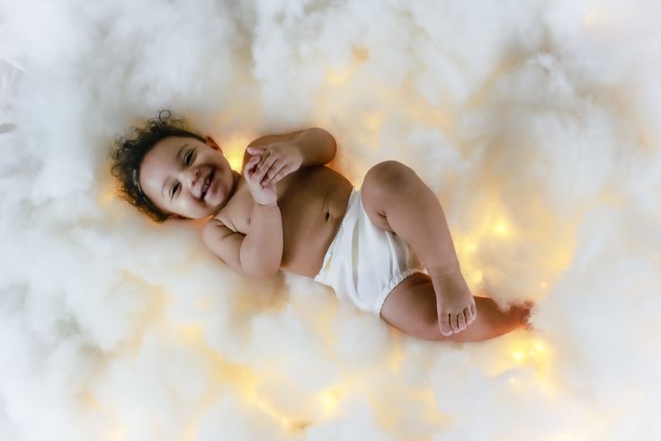 a baby is laying down on some fluffy white clouds and smiling at the camera while wearing a diaper