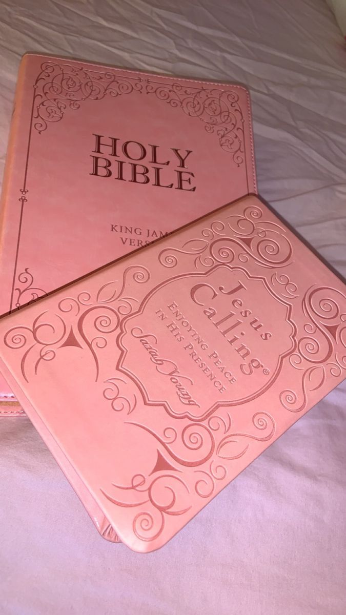 two pink bibles sitting on top of a bed next to each other in front of a pillow