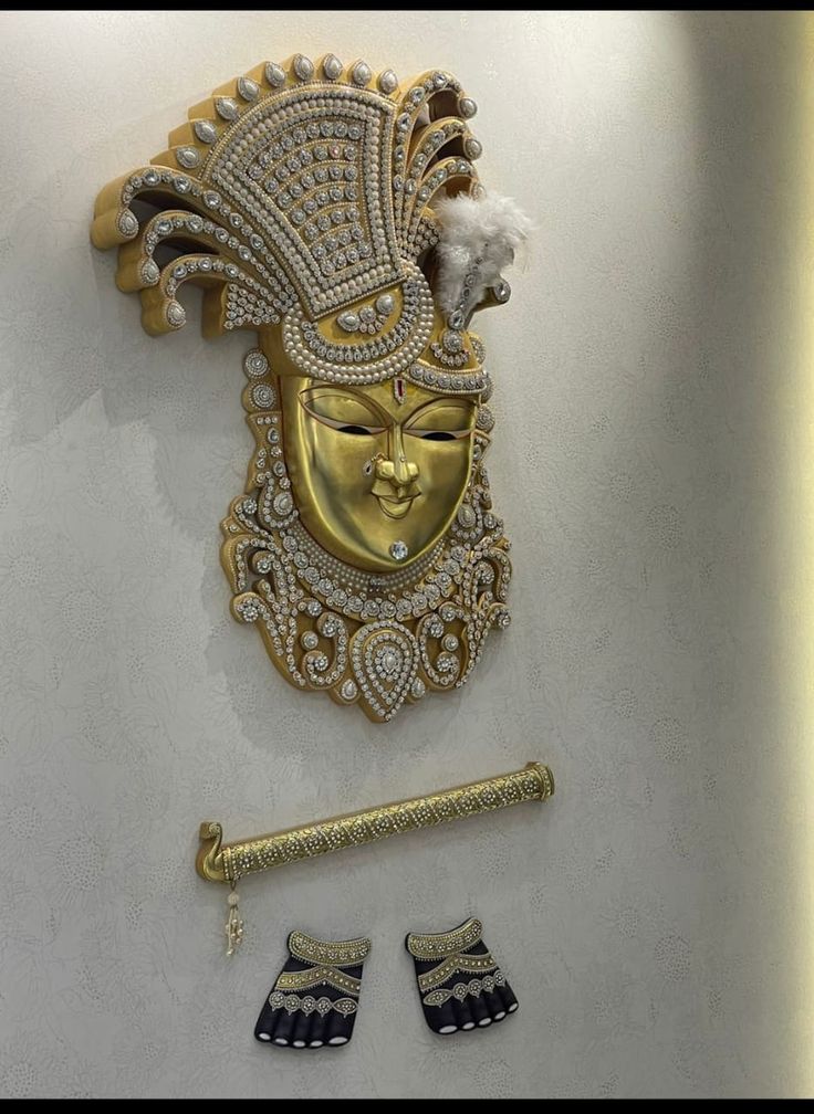 a gold mask and two pairs of earrings are displayed on a white wall next to a pair of silver shoes