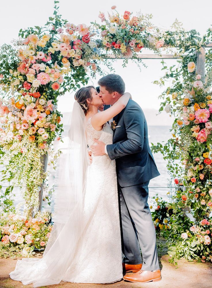 a bride and groom kissing under an arch of flowers