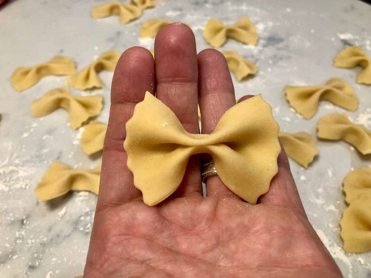 a hand holding a small yellow bow on top of some pasta shells in the background